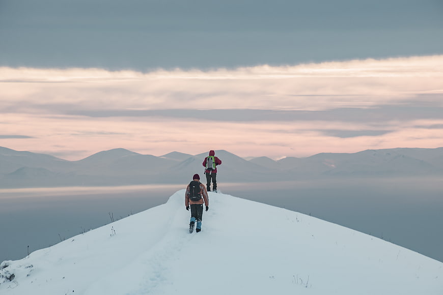 Two hikers walking on snowy mountain ridge at sunset