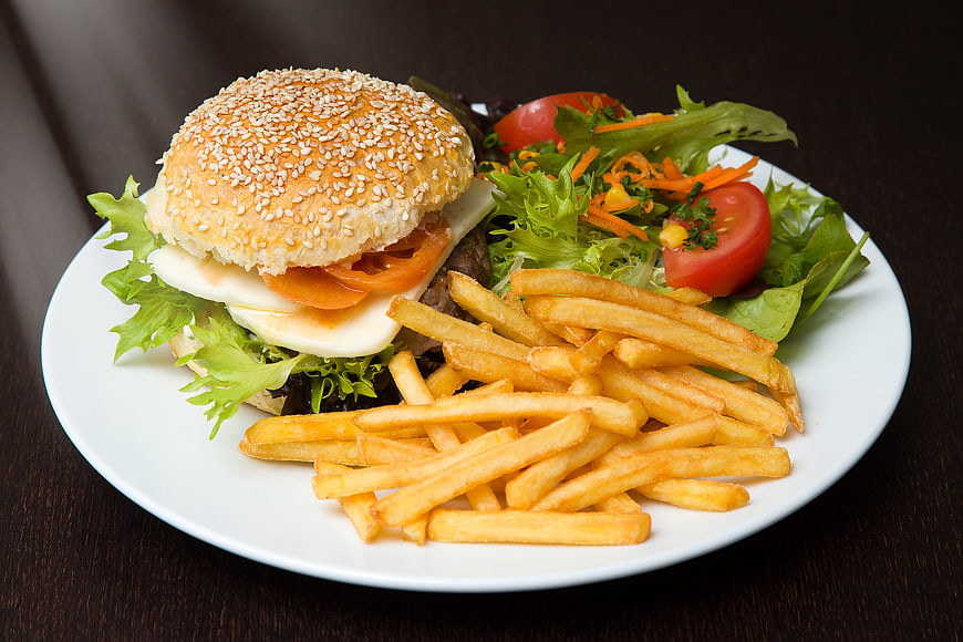 Delicious burger with fries and salad on a white plate