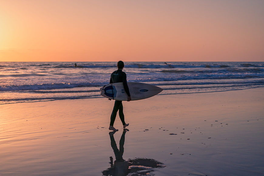Surfer Walking on Beach at Sunset with Surfboard