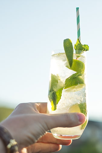 Hand holding refreshing mojito cocktail with mint and lime
