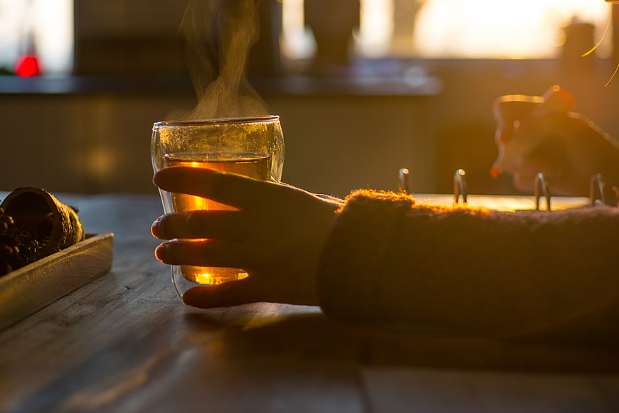 Hand holding steaming tea glass in warm sunlight
