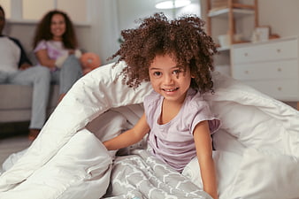 Happy young girl with curly hair playing in a duvet fort