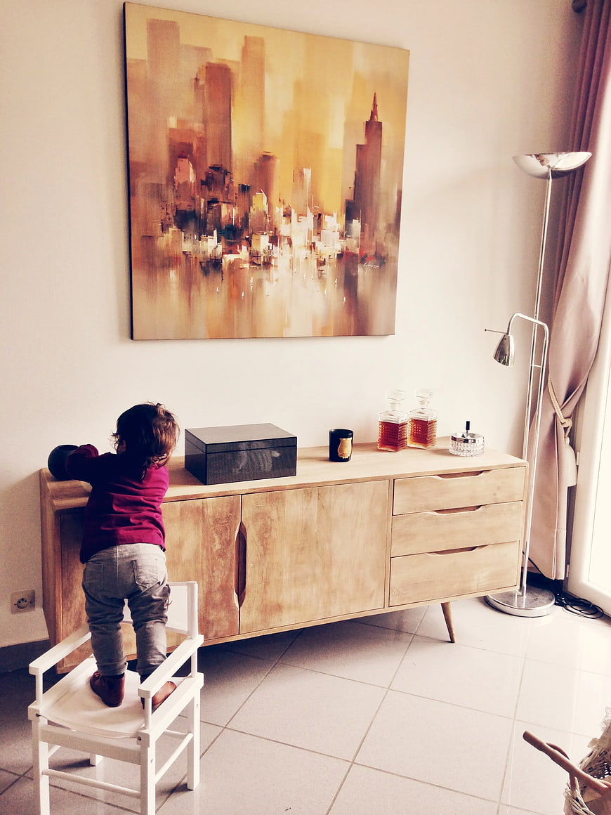 Toddler standing on chair reaching for sideboard in living room