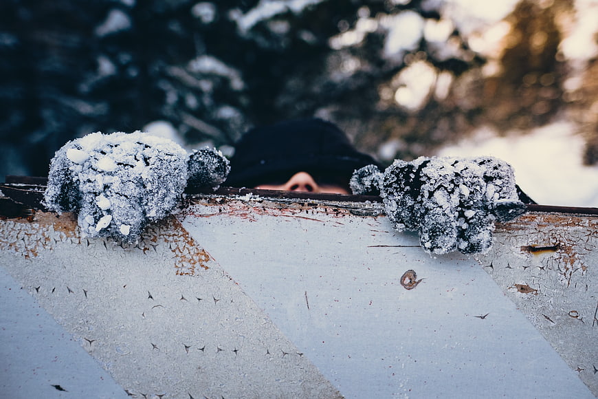 Man in Snowy Gloves Peeking Over Rusty Fence