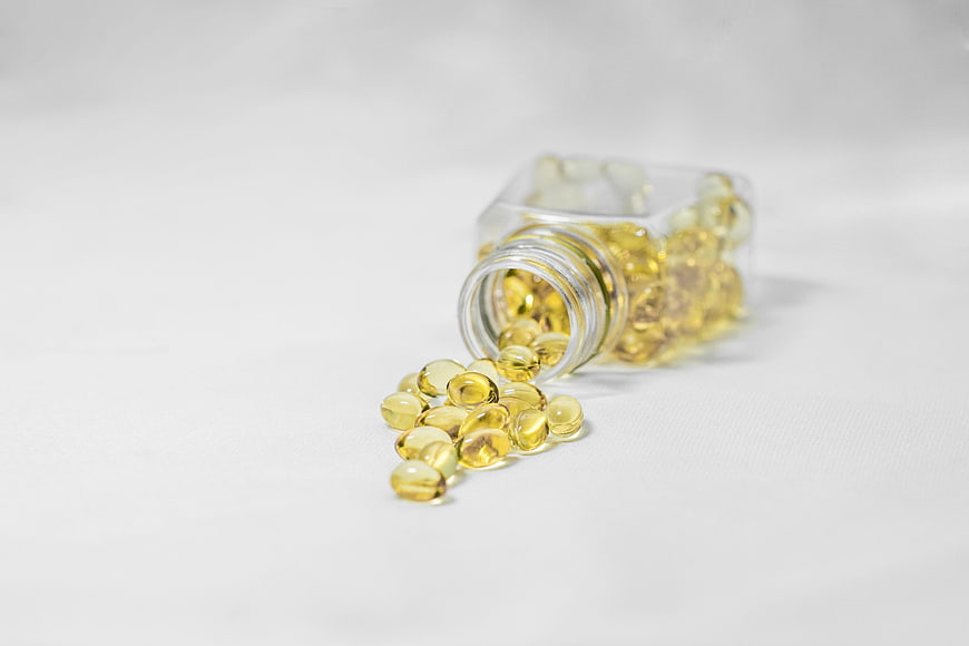 Spilled Yellow Vitamin Capsules From Glass Bottle On White Background