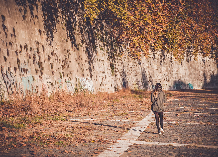 Woman Walking Away on Autumn Path Near Concrete Wall