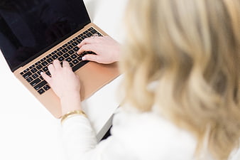 Over-the-shoulder view of woman typing on gold laptop