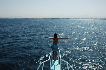 Woman Standing On Boat Bow With Arms Outstretched Over Ocean