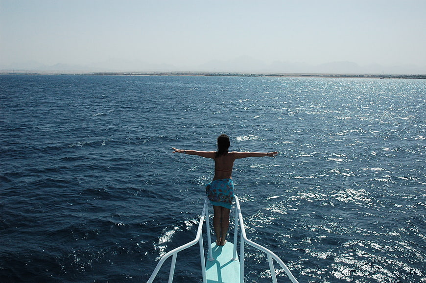 Woman Standing On Boat Bow With Arms Outstretched Over Ocean