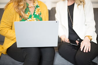 Two women collaborating on laptop and smartphone on sofa