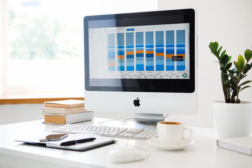 Modern white office desk with Mac computer displaying analytics charts