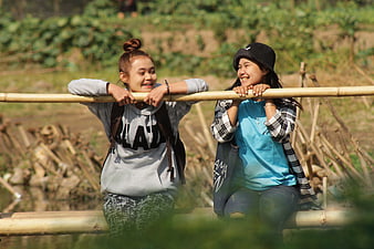 Two smiling young women sitting on a bamboo bridge outdoors