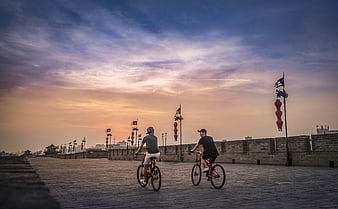 Two Cyclists Riding on Ancient City Wall at Sunset