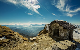 Rustic stone hut on snowy mountain peak with panoramic valley view