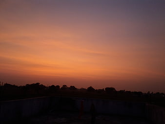 Vibrant orange and purple sunset sky over dark silhouette landscape
