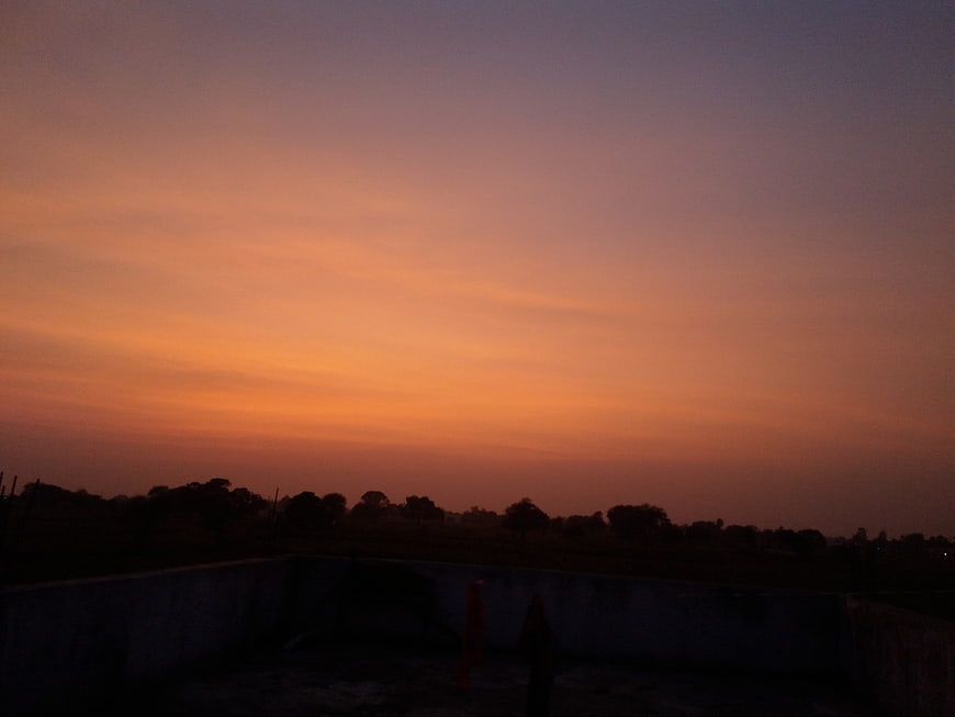 Vibrant orange and purple sunset sky over dark silhouette landscape