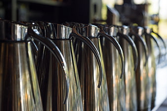 Row of shiny metal coffee pitchers in a cafe