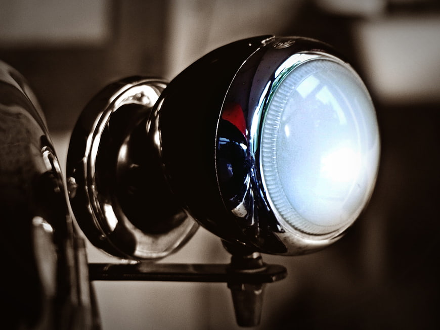Close-up of vintage chrome car headlight with glowing bulb