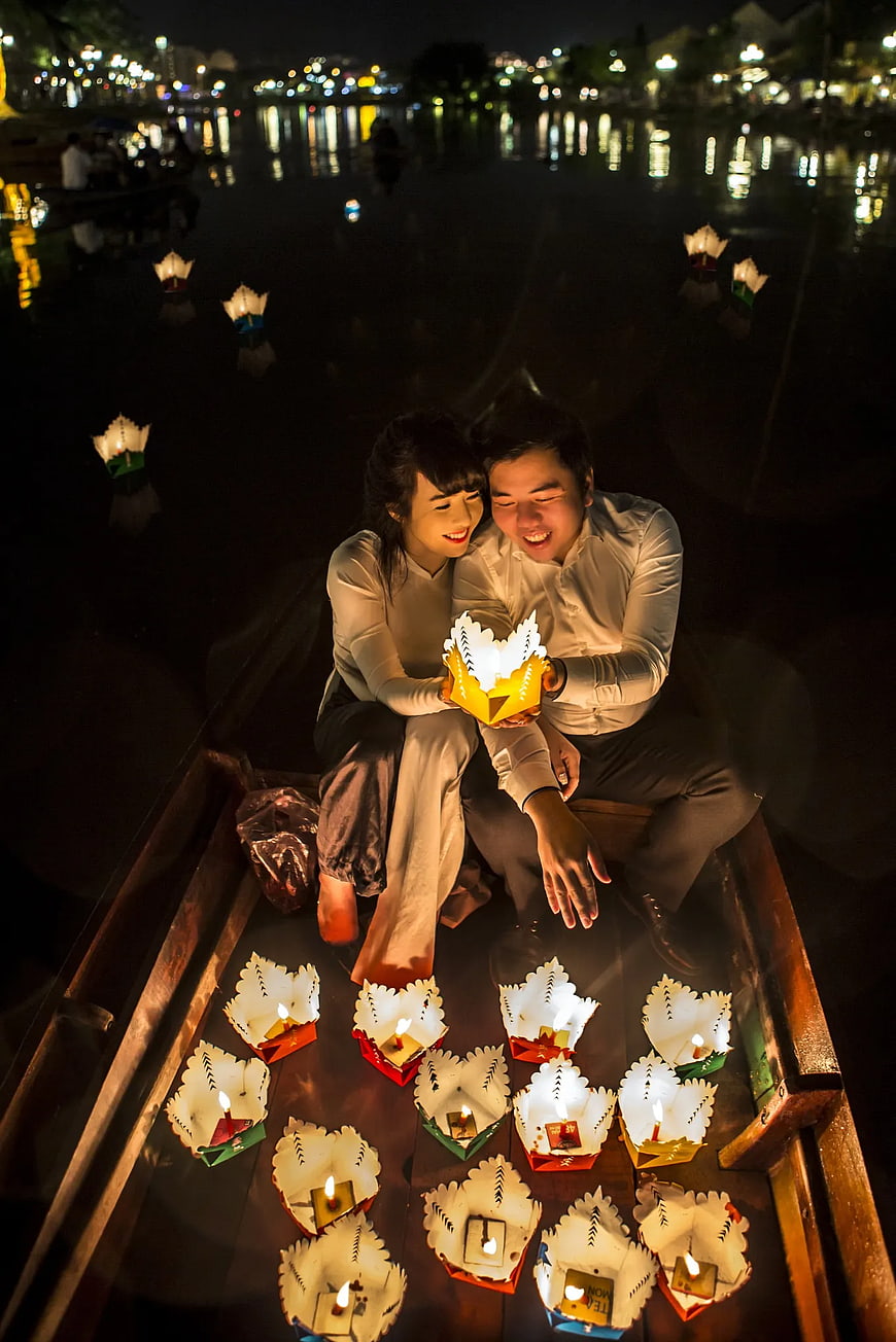 Couple holding glowing lotus lantern on boat at night