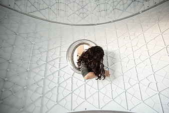 Woman with curly hair looking through circular window in geometric white structure