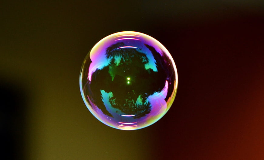 Iridescent soap bubble reflecting nature against dark background