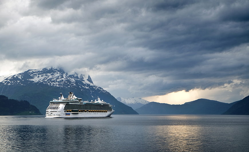 Cruise Ship Sailing Past Snowy Mountains Under Dramatic Clouds