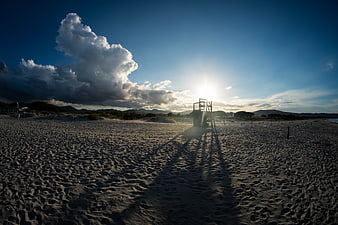 Lifeguard tower on sandy beach with dramatic clouds and sunset