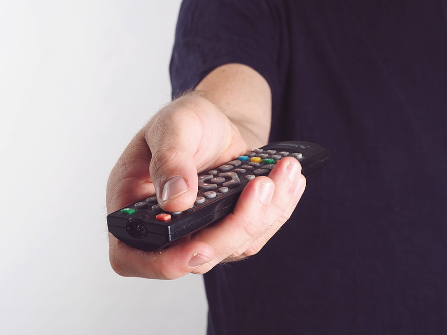 Hand Holding Black TV Remote Control on White Background