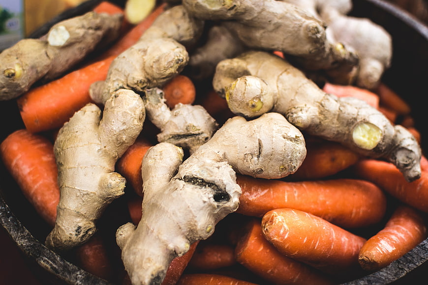 Fresh ginger root and carrots in a rustic wooden bowl
