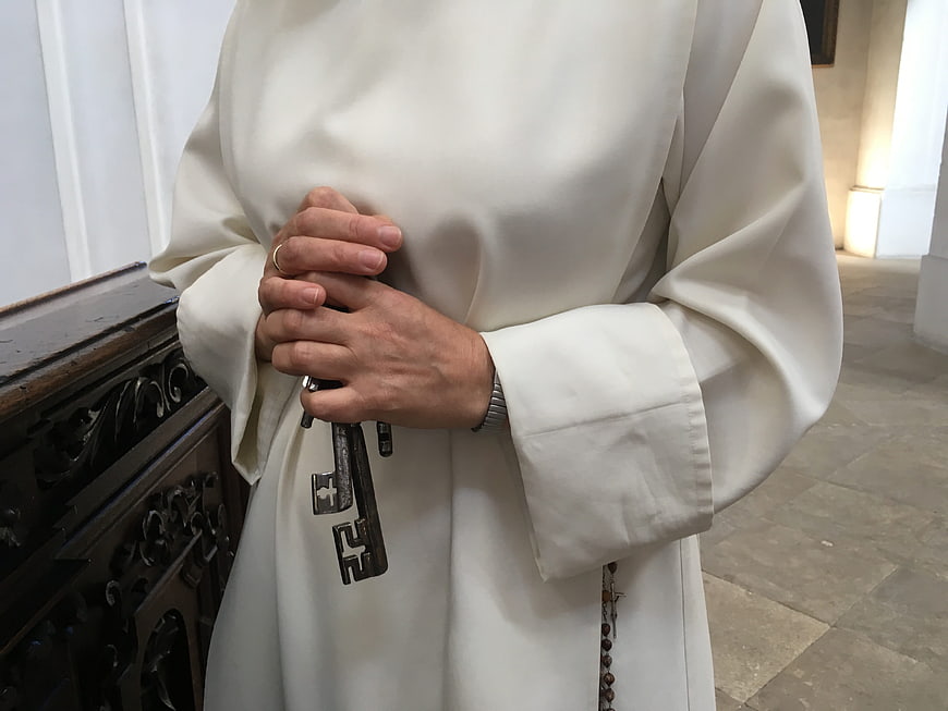 Priest holding keys in white robe indoors