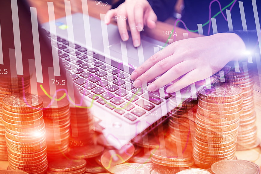 Hands typing on laptop with coins and financial charts overlay