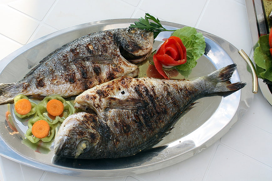 Grilled Whole Fish Dish With Vegetable Garnish On Silver Platter