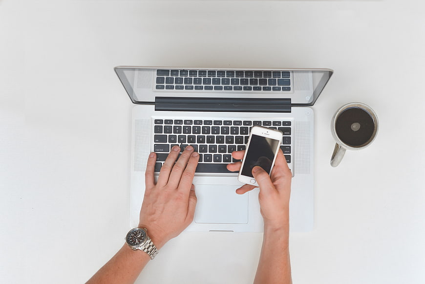 Top view of hands typing on laptop and holding smartphone with coffee