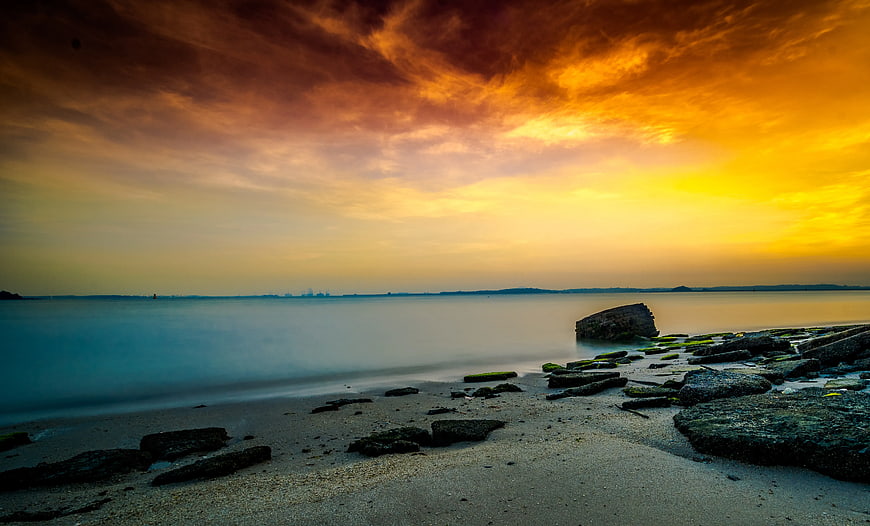 Dramatic sunset over rocky shoreline with long exposure water