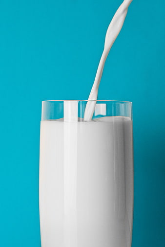 Fresh milk pouring into a glass on a blue background