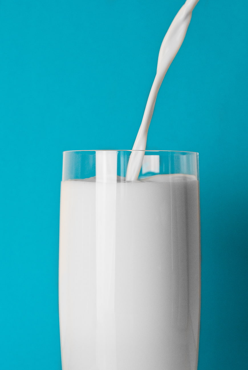 Fresh milk pouring into a glass on a blue background