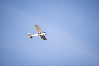 Small white airplane flying against clear blue sky