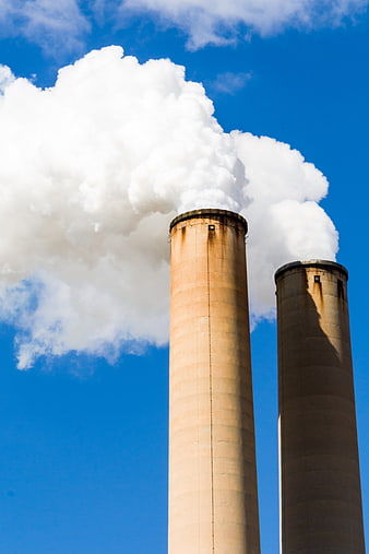 Two Industrial Smokestacks Emitting White Smoke Against Blue Sky