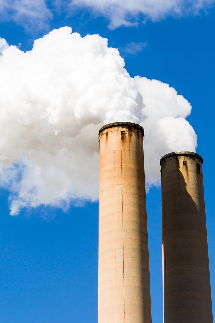 Two Industrial Smokestacks Emitting White Smoke Against Blue Sky