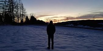 Silhouette of person standing on frozen lake at sunset
