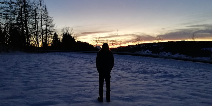 Silhouette of person standing on frozen lake at sunset