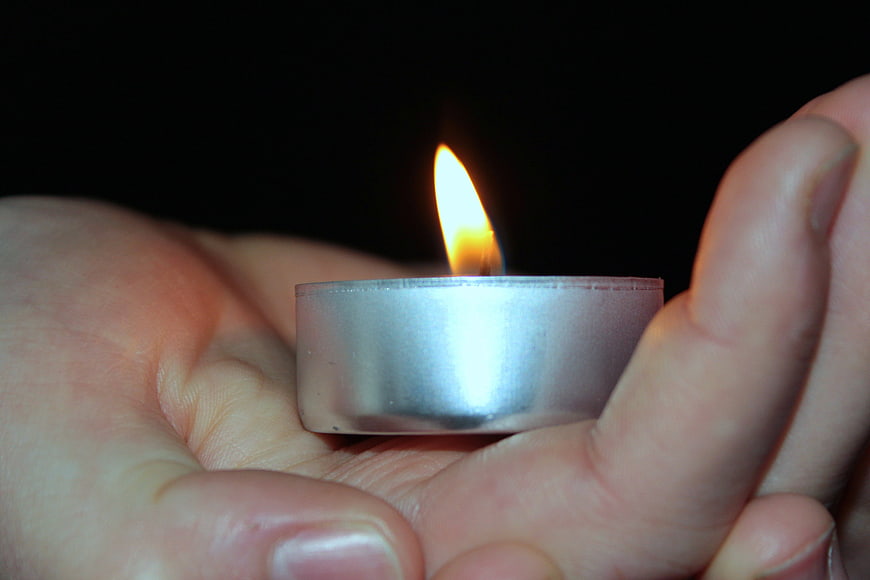 Close-up of hands holding a lit tea light candle in the dark
