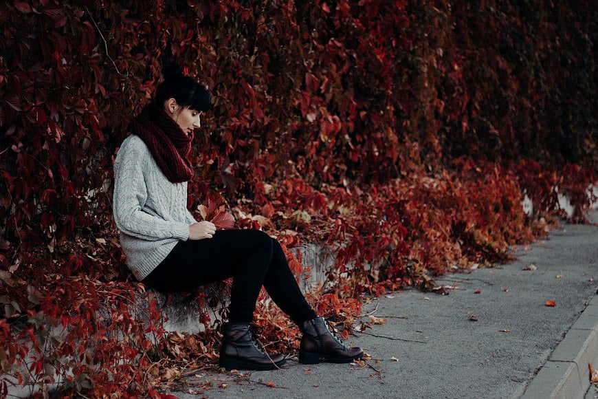 Woman Sitting on Wall Surrounded by Red Autumn Leaves