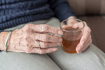 Close-up of elderly woman's hands holding a glass cup of tea