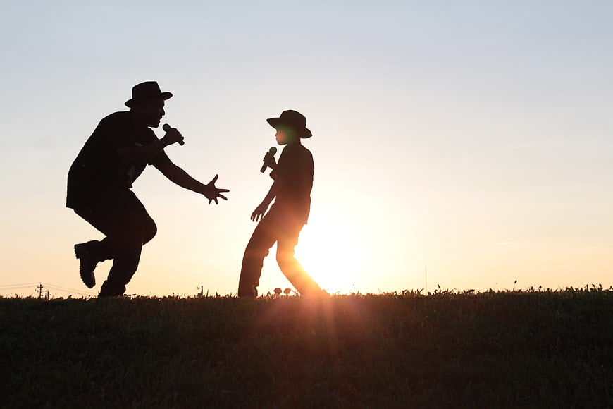 Silhouette of father and son singing with microphones at sunset
