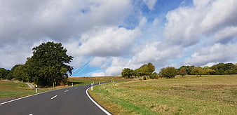 Winding country road through green fields under cloudy blue sky