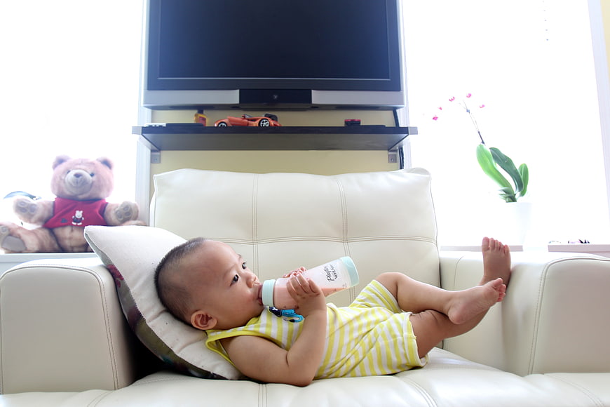 Baby drinking milk bottle on white sofa