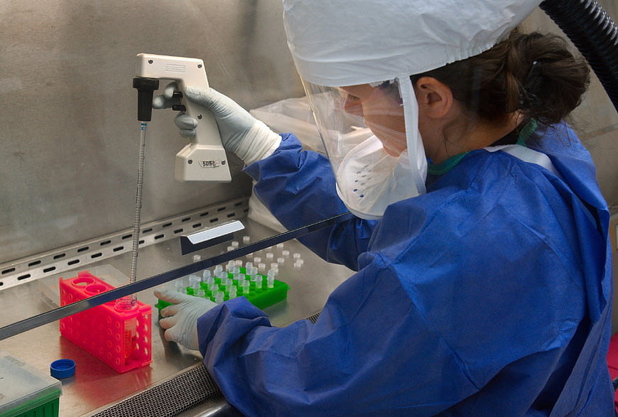 Female scientist in protective gear using pipette in laboratory