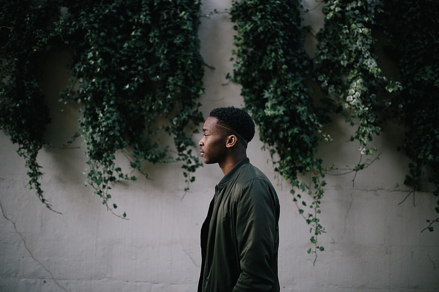 Profile of Young Black Man Standing Against Ivy Wall