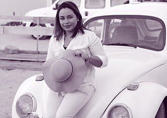 Woman with hat leaning on vintage white car